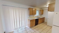This two-floor residence offers a practical and well-organized layout designed for comfortable everyday living. The main level features an open living area with rich hardwood-style flooring, baseboard heating, and a large window that allows ample natural light to fill the space. A front entry door with a transom window provides a welcoming arrival, and a staircase with a railing leads to the upper floor. The kitchen is equipped with warm wood cabinetry, light countertops, a built-in dishwasher, and a sink beneath a window, complemented by light tile flooring and vertical blinds covering a large sliding glass door. A half bathroom on the main level features tile flooring and clean, white fixtures. Upstairs, the bedrooms are carpeted and bright, each featuring windows with blinds and baseboard heating units that run along the walls, ensuring warmth throughout. A full bathroom on the upper level includes a tiled shower-tub combination with white fixtures. Throughout the home, the neutral white walls provide a clean, versatile backdrop. Baseboard heating is present throughout both floors, and a wall-mounted air conditioning unit on the main level ensures year-round comfort. The overall ambiance is clean, functional, and move-in ready.