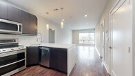 This well-appointed 2-bedroom, 1-bathroom unit offers a thoughtfully designed single-floor layout with a cohesive modern aesthetic throughout. Rich, dark hardwood flooring flows seamlessly across every room, providing warmth and continuity. The open-concept kitchen and living area serves as the heart of the space, where a sleek kitchen island with white quartz countertops anchors the room. Dark espresso cabinetry is paired with a full suite of stainless steel appliances, including a double oven range, built-in microwave, and a side-by-side refrigerator. Stylish pendant lighting hangs above the island, adding a refined touch. The living area extends naturally toward large windows and a sliding glass door that invite generous natural light and offer views of the surrounding cityscape. Both bedrooms are generously proportioned, featuring the same handsome hardwood floors, ceiling fans, and ample closet space. The primary bedroom includes a sliding glass door for additional outdoor access and natural light. The bathroom is a standout feature, showcasing floor-to-ceiling marble-style tile in the walk-in shower, complete with built-in shelving niches and a modern multi-function showerhead. A dedicated laundry area rounds out the functional layout of this contemporary urban residence.