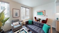 This single-floor unit offers a thoughtfully designed layout that maximizes functionality within a compact footprint. The living area serves as the heart of the space, featuring large windows that invite abundant natural light and provide views of the surrounding building exterior. Neutral wall tones and light-colored ceilings enhance the sense of openness, while the room comfortably accommodates a seating arrangement alongside a small dining area.

The galley-style kitchen is efficiently organized, featuring stainless steel appliances, including a range, dishwasher, and built-in microwave. White upper cabinetry pairs with warm wood-toned lower cabinets, complemented by a textured subway tile backsplash and grey composite countertops. A stacked washer and dryer unit is conveniently integrated into the kitchen corridor, adding practical in-unit laundry access.

Dark hardwood-style flooring runs through the kitchen and connecting hallway, transitioning to a carpeted or area-rug-defined living space. The bathroom is clean and straightforward, featuring a full-size soaking tub with a shower, chrome fixtures, and a patterned shower curtain that adds a subtle design accent. Overall, the unit balances modern finishes with practical, day-to-day livability.