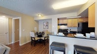 This single-story residence offers a well-organized layout that connects its primary living spaces in a practical and functional flow. The living room serves as the heart of the home, featuring hardwood-style flooring, a ceiling fan, and a large window that allows natural light to fill the space. Neutral-toned walls and a textured ceiling contribute to the room's understated, comfortable ambiance.

Adjacent to the living area, the dining space is defined by a dedicated nook with a slightly varied ceiling treatment, creating a sense of separation while maintaining an open connection to the rest of the common areas. The galley-style kitchen is efficiently designed with warm wood cabinetry, dark countertops, a stainless steel sink, and black appliances including a range, refrigerator, and dishwasher. A breakfast bar with seating bridges the kitchen and dining areas.

The bedrooms feature plush carpeting, neutral walls, and generous closet space, including a walk-in closet in one room. Windows with curtains provide natural light and privacy. The bathroom is well-appointed with wood cabinetry, a dark countertop, a full tub-shower combination, and hardwood-style flooring, rounding out this cohesive and functional residence.