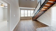 This two-bedroom, two-bathroom residence with a loft showcases a compelling mix of industrial character and contemporary design across two floors. The kitchen serves as a standout feature, boasting exposed wooden beams, corrugated metal ceiling details, and Edison bulb pendant lighting that lend a warm, loft-style aesthetic. Two-toned cabinetry pairs white upper cabinets with slate-gray lower ones, complemented by granite countertops, a subway tile backsplash, stainless steel appliances, and a central island with additional storage. Dark hardwood flooring anchors the space with rich contrast.

The main living area features soaring ceilings, large windows that draw in natural light, and an open-riser staircase with a sleek black metal frame and wood treads, leading to the upper loft level. Both bedrooms are carpeted and include ceiling fans, with windows providing natural light. One bathroom features a tiled tub-shower combination with built-in shelving, while the second offers a glass-enclosed walk-in shower with tile surround and marble-style flooring. Neutral tones throughout create a clean, versatile backdrop suited to a variety of interior styles.