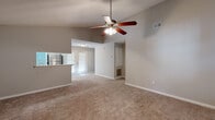 This single-story residence offers a well-organized layout with distinct living, kitchen, and bedroom zones. The living area is a standout space, featuring soaring vaulted ceilings that lend an open, airy quality, complemented by a ceiling fan with integrated lighting. Neutral-toned carpet runs throughout the living and bedroom areas, creating a cohesive look. A pass-through window connects the living room to the kitchen, enhancing the sense of openness between the two spaces.

The kitchen is equipped with stainless steel appliances, including a refrigerator, range, and over-the-range microwave. White cabinetry with light wood accents provides ample storage, while light-toned wood-look flooring adds a clean, practical finish. A built-in sink and dishwasher complete the functional layout.

The bedrooms are generously sized, each featuring plush carpeting, ceiling fans, and windows that allow natural light to filter in. Crown molding is present in at least one bedroom, adding a refined architectural detail. Built-in cabinetry is also visible in the living area, offering additional storage.

The two bathrooms feature wood-look tile flooring, light wood vanities with white countertops, and large mirrors. One bathroom includes a full tub-shower combination, while the other serves as a half or three-quarter bath. The overall palette throughout is neutral and understated, creating a clean, move-in ready environment.