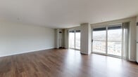Located at 1 Park Row W in the heart of Providence, Rhode Island, this single-floor residence offers a thoughtfully designed layout with a clean, contemporary aesthetic throughout. The expansive main living area is immediately striking, defined by rich, dark hardwood-style flooring and crisp white walls that create a bright, neutral canvas. Multiple large sliding glass doors open to balcony access, flooding the space with natural light and framing elevated views of the surrounding Providence cityscape and neighborhoods. The open layout allows for flexible use of the generous living and dining areas. The kitchen is outfitted with white shaker-style cabinetry, light quartz countertops, a stainless steel undermount sink, and a bold dark subway tile backsplash, complemented by stainless steel appliances including a dishwasher. The bedrooms are well-proportioned, featuring the same hardwood-style flooring and ample closet space with bifold doors. Two full bathrooms include tub-shower combinations with curved chrome curtain rods, vanities with mirrors, and wood-look flooring. Additional features include ceiling-mounted HVAC vents and generously sized windows that extend the sense of openness throughout every room.