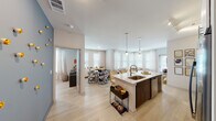 This single-floor residence in Pensacola, Florida offers a thoughtfully designed open-concept layout that seamlessly connects the kitchen, dining, and living areas. The kitchen is a standout feature, outfitted with stainless steel appliances, two-tone cabinetry pairing white upper cabinets with dark lower cabinets, a quartz countertop island with an undermount sink, and elegant pendant lighting. Light wood-style flooring runs throughout the main living areas, enhancing the bright and airy atmosphere created by an abundance of natural light from multiple windows. The living room benefits from a striking bay window configuration with sheer curtains and blinds, flooding the space with sunlight. A welcoming entryway corridor leads into the heart of the home. The primary bedroom features a ceiling fan, a window with blinds, and plush carpeting, while a second bedroom offers a similarly comfortable and well-lit environment with a ceiling fan. Both bathrooms are finished with quartz vanity countertops, dark wood cabinetry, large mirrors, and tub-shower combinations with tiled surrounds. Throughout, the neutral color palette and clean architectural lines contribute to a cohesive, contemporary aesthetic well-suited for comfortable everyday living.