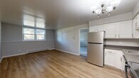 Located at 110 Colleen Rd in Troy, NY, this efficient one-bedroom, one-bathroom unit offers a well-organized layout across a single floor. The open-concept kitchen and living area serves as the heart of the home, featuring light hardwood-style flooring, neutral gray walls, and a stylish chandelier overhead. The kitchen is well-appointed with white shaker cabinetry, dark countertops, and a full suite of stainless steel appliances including a refrigerator, dishwasher, electric range, and microwave. Baseboard heating runs throughout, ensuring year-round comfort. The living area is bright and airy, benefiting from natural light through windows that frame views of surrounding greenery. The spacious primary bedroom is carpeted for comfort and offers generous proportions, built-in shelving, and large windows that invite additional natural light. A dedicated closet provides practical storage. The bathroom features a clean, full-sized soaking tub and shower combo with tiled surround. The entry area includes hardwood-style flooring and a baseboard heater. Clean finishes and a neutral palette throughout make this a move-in-ready space in a convenient Troy location.