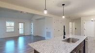 Located at 1025 Retreat Dr in Bartow, Florida, this single-story home offers a thoughtfully designed open-concept floor plan encompassing 2 bedrooms, 3 bathrooms, and dedicated spaces for laundry, storage, and more. The living room is a standout area, featuring soaring vaulted ceilings, a ceiling fan, gleaming wood-look hard flooring, and multiple windows alongside a rear door that fills the space with natural light and outdoor views. The kitchen is outfitted with rich dark-brown cabinetry, stainless steel appliances including a side-by-side refrigerator with ice maker, an electric range, and a built-in microwave. A central island with granite countertops and pendant lighting above serves as both a functional workspace and a focal point of the open living area. Wood-look flooring flows seamlessly throughout the main living areas and hallways, while the bedrooms are finished with plush carpeting. The generously sized primary bedroom includes a ceiling fan and a large window with outdoor views, accompanied by a spacious walk-in closet with wire shelving. The dedicated laundry room features wire shelving and hookups for both washer and dryer. Clean white walls, panel-style doors with matte black hardware, and consistent finishes throughout lend the home a cohesive, modern aesthetic.