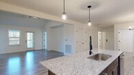 Located at 1025 Retreat Dr in Bartow, Florida, this single-story home offers a thoughtfully designed open-concept floor plan encompassing 2 bedrooms, 3 bathrooms, and dedicated spaces for laundry, storage, and more. The living room is a standout area, featuring soaring vaulted ceilings, a ceiling fan, gleaming wood-look hard flooring, and multiple windows alongside a rear door that fills the space with natural light and outdoor views. The kitchen is outfitted with rich dark-brown cabinetry, stainless steel appliances including a side-by-side refrigerator with ice maker, an electric range, and a built-in microwave. A central island with granite countertops and pendant lighting above serves as both a functional workspace and a focal point of the open living area. Wood-look flooring flows seamlessly throughout the main living areas and hallways, while the bedrooms are finished with plush carpeting. The generously sized primary bedroom includes a ceiling fan and a large window with outdoor views, accompanied by a spacious walk-in closet with wire shelving. The dedicated laundry room features wire shelving and hookups for both washer and dryer. Clean white walls, panel-style doors with matte black hardware, and consistent finishes throughout lend the home a cohesive, modern aesthetic.