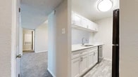 Located at 2509 N Forty Circle in Arlington, Texas, this single-floor, two-bedroom, two-bathroom residence offers a well-organized layout designed for comfortable everyday living. The open-concept kitchen and living area form the heart of the home, where a pass-through counter connects the kitchen to the living space, creating an inclusive and social atmosphere. The kitchen is outfitted with crisp white cabinetry, light countertops, a stainless steel sink, and black appliances including a refrigerator and range, all complemented by wood-look flooring. Soft, neutral-toned carpet extends throughout the living and bedroom areas, lending warmth and comfort underfoot. The spacious primary bedroom features a ceiling fan with light fixture and sliding glass doors that invite natural light and provide outdoor access. The second bedroom also offers a ceiling fan and a window with views of surrounding greenery. Both bedrooms are served by dedicated closets with built-in shelving, maximizing storage. Each bathroom is appointed with a full tub-shower combination, white tile surround, wood-look tile flooring, and a vanity with light countertops. Textured ceilings and neutral wall tones throughout contribute to a clean, cohesive aesthetic across the entire residence.