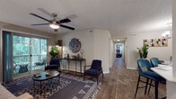 This single-floor residence offers a thoughtfully designed layout that balances comfort and functionality across its well-proportioned rooms. The living area serves as the heart of the home, featuring wood-look flooring, a ceiling fan, and a sliding glass door that opens to a private outdoor balcony framed by lush greenery — filling the space with natural light and views of surrounding trees. A dedicated dining area sits adjacent, finished with the same wood-look flooring, chair rail molding, and an understated chandelier overhead.

The galley-style kitchen is efficiently arranged with white upper cabinetry, gray lower cabinetry, white countertops, a subway tile backsplash, stainless steel appliances, and wood-look flooring — offering ample storage and workspace. A long hallway connects the living areas to the private quarters, which include multiple bedrooms carpeted for comfort. Each bedroom features natural light from window blinds and closet storage. One bedroom is well-suited as a home office or secondary sleeping space.

Two full bathrooms serve the residence, each featuring wood-look tile flooring, a vanity with storage, and clean, neutral finishes. One includes a tub-shower combination, while the other provides a more refined vanity setup. Throughout, the neutral color palette and consistent flooring selections create a cohesive, modern ambiance.