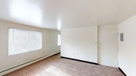 This single-floor residential unit offers a straightforward and functional layout designed for comfortable everyday living. The living area is generously proportioned, featuring neutral wall-to-wall carpeting, white walls, and multiple windows fitted with blinds that allow ample natural light to fill the room. A baseboard heating system runs along the perimeter, ensuring efficient climate control throughout. The space benefits from a clean, open feel with dark baseboards providing a subtle contrast to the light-toned carpet and walls.

The kitchen is efficiently organized, featuring white cabinetry both above and below the countertops, warm wood-toned laminate counters, and a stainless steel sink. Vinyl plank flooring extends throughout the kitchen, complementing the white appliances including a refrigerator and range. Upper shelving adds additional storage convenience.

The bedrooms are well-sized, each with carpeted floors, white walls, and windows that invite natural light. One bedroom includes a closet with a rod, providing built-in storage. The bathroom is equipped with a full-sized soaking tub and shower combination, a pedestal sink, a small privacy window, and vinyl plank flooring, maintaining a clean and utilitarian aesthetic consistent with the rest of the unit.