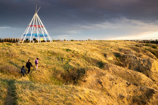A family walks outdoors along a hiking trail in Seven Persons Coulee by the Saamis Tepee at sunset.