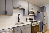 Located at 4200 N Carlin Springs Rd in Arlington, VA, this one-bedroom, one-bathroom unit offers a thoughtfully designed layout across a single floor. The open-concept living and dining area is bright and airy, highlighted by light wood-style flooring, a ceiling fan, and a large window that invites natural light and outdoor views. The modern kitchen is a standout feature, showcasing sleek gray cabinetry with matte black hardware, white quartz countertops, a white subway tile backsplash, and a full suite of stainless steel appliances including a refrigerator, electric range, and over-the-range microwave. A matte black spring-neck faucet adds a contemporary accent to the undermount sink. The bedroom is carpeted for comfort, features a window with exterior views, and includes a sliding double-panel closet for convenient storage. The bathroom is finished with large-format tile flooring, a gray vanity with black fixtures, and a tub-shower combination with marble-look tile surround. An in-unit laundry area and dedicated closet space add to the unit's practical appeal. The clean, neutral palette and modern finishes throughout create a cohesive and move-in-ready living environment.