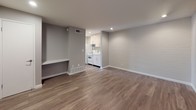 This single-floor unit offers a clean, modern aesthetic throughout, combining practical design with thoughtful finishes. The living area is bright and open, featuring warm hardwood-style flooring that extends seamlessly through the space, painted brick accent walls that add texture and character, and recessed lighting that provides even illumination. A built-in ledge along one wall offers a convenient surface for storage or display. Natural light enters through a large window dressed with vertical blinds, and a glass-panel entry door further enhances the sense of openness.

The compact kitchen is efficiently laid out and equipped with white cabinetry, light-toned countertops, a stainless steel sink, and white appliances including a refrigerator, electric range, and overhead microwave. The cabinetry provides ample storage with both upper and lower units.

The bedroom is generously proportioned, featuring the same hardwood-style flooring, a painted brick accent wall, and a large window that brings in natural light and exterior views. A pair of built-in closets with sliding doors offers substantial storage capacity.

The bathroom is finished with large-format, linear-textured tiles in a neutral grey tone, and includes a combined tub and shower with a glass sliding door and a handheld showerhead, creating a clean and contemporary feel throughout.