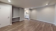 This single-floor unit offers a clean, modern aesthetic throughout, combining practical design with thoughtful finishes. The living area is bright and open, featuring warm hardwood-style flooring that extends seamlessly through the space, painted brick accent walls that add texture and character, and recessed lighting that provides even illumination. A built-in ledge along one wall offers a convenient surface for storage or display. Natural light enters through a large window dressed with vertical blinds, and a glass-panel entry door further enhances the sense of openness.

The compact kitchen is efficiently laid out and equipped with white cabinetry, light-toned countertops, a stainless steel sink, and white appliances including a refrigerator, electric range, and overhead microwave. The cabinetry provides ample storage with both upper and lower units.

The bedroom is generously proportioned, featuring the same hardwood-style flooring, a painted brick accent wall, and a large window that brings in natural light and exterior views. A pair of built-in closets with sliding doors offers substantial storage capacity.

The bathroom is finished with large-format, linear-textured tiles in a neutral grey tone, and includes a combined tub and shower with a glass sliding door and a handheld showerhead, creating a clean and contemporary feel throughout.