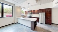 Located at 112 Wayne Ave in Dayton, Ohio, this single-floor unit offers a thoughtfully designed layout with a distinctly modern, industrial aesthetic. Polished concrete floors run continuously throughout the space, complementing exposed concrete ceilings and painted masonry block walls that lend an urban character to the interior.

The kitchen is a standout feature, equipped with rich dark-wood cabinetry, white countertops, and a full suite of stainless steel appliances including an electric range, microwave, refrigerator, and dishwasher. A peninsula with an integrated sink provides additional workspace and casual seating. Pendant lighting above adds warmth and visual interest to the area.

The living and bedroom spaces are generously proportioned, each featuring black-framed windows that bring in natural light and views of the surrounding urban landscape. Wall-mounted mini-split HVAC units and ceiling fans ensure year-round comfort. The bathroom is clean and functional, outfitted with a tub/shower combination, white surrounds, dark fixture hardware, and a dark-wood vanity with a white countertop.

A dedicated laundry area houses a full-size Whirlpool washer and dryer, adding practical convenience to the unit's modern amenities.
