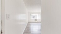 Located at 10237 Western Avenue in Downey, California, this single-floor, one-bedroom, one-bathroom unit offers a clean and modern living environment with thoughtfully updated finishes throughout. Light wood-style flooring runs continuously across all rooms, creating a cohesive and airy feel that maximizes the sense of space.

The living area is bright and open, benefiting from a large window dressed with vertical blinds that invites natural light. A wall-mounted air conditioning unit and an in-unit heater provide year-round climate control. The textured ceiling adds a classic touch to the otherwise contemporary interior.

The kitchen is a standout feature, showcasing gray shaker-style cabinetry with matte black hardware, light countertops, a stainless steel sink with a modern faucet, and a full suite of stainless steel appliances including a refrigerator and range. Additional white cabinetry provides generous storage just outside the kitchen area.

The bedroom offers a comfortable, well-proportioned layout highlighted by a built-in closet system featuring full-length mirrored sliding doors topped with white upper cabinets, providing ample storage and enhancing the sense of depth in the room.

The bathroom is finished in an all-white palette with tile-surround tub and shower, a white vanity with cabinet storage, and a small window for ventilation and natural light. A hallway connects the rooms, completing this efficiently designed and move-in ready unit.