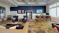 Located at 7 Archstone Ave in Tewksbury, Massachusetts, this single-floor clubhouse-style community space is thoughtfully designed with a bold, contemporary aesthetic. The interior is defined by striking navy blue accent walls paired with crisp white wainscoting and coffered or tray ceiling details, creating a polished yet inviting atmosphere throughout.

The main lounge area is generously proportioned, furnished with a mix of plush sofas, wingback chairs, and a central coffee table, all set atop a richly patterned mosaic-style floor. A wall-mounted flat-screen display and a high-top bar table with leather stools make this an ideal gathering and social hub. Adjacent to the lounge, a dedicated workspace features desks, office chairs, and an eye-catching patterned feature wall, providing a functional environment for residents.

A welcoming entry foyer includes a leather bench and decorative accents, with direct access to the outdoors through glass-paneled doors that flood the space with natural light. The game room is a standout feature, anchored by a full-size pool table and a stone-surround fireplace framed by a dramatic floor-to-ceiling metal panel wall. Large transom windows in this area offer serene views of the surrounding tree line. Cozy seating nooks with wingback chairs are positioned throughout, inviting relaxed conversation and leisure.