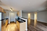 This two-bedroom, two-bathroom residence at 100 Thompson Farm Rd in Bedford, Massachusetts offers a thoughtfully arranged single-floor layout with a clean, neutral aesthetic throughout. The open-concept kitchen, dining, and living area forms the heart of the home, featuring wood-look flooring, light maple cabinetry, dark granite countertops, a peninsula with a sink, and stainless steel appliances including a refrigerator, range, and microwave. A track lighting fixture illuminates the kitchen, which flows seamlessly into the spacious living and dining areas. The living room provides generous proportions with rich hardwood-style flooring and a bright, airy feel. Both bedrooms are carpeted for comfort, with the primary bedroom offering a notably generous footprint. The second bedroom features a large window that invites natural light and outdoor views. Two full bathrooms are finished with wood-look flooring, white cabinetry, granite-topped vanities, and tub-shower combinations. A dedicated in-unit laundry area with wire shelving adds everyday convenience. Six closets are distributed throughout the home, providing exceptional storage. The hallway connects all areas efficiently, and the overall design presents a clean, move-in-ready living environment.