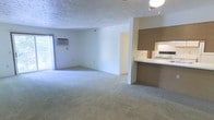 This single-floor residence features two bedrooms and one bathroom within a well-utilized floor plan. The open living and dining area is spacious and carpeted, providing a neutral, move-in-ready canvas with light-toned walls that brighten the space. A window unit air conditioner and a sliding glass door or large window allow for natural light and ventilation in the main living area, lending a sense of openness to the room.

Adjacent to the living space, the kitchen is accessible via a pass-through counter with a built-in breakfast bar, creating a convenient connection between the cooking and living areas. The kitchen features wood-toned upper cabinetry, a white range, and a mirrored backsplash element that adds depth to the compact cooking space. The textured ceiling throughout the home adds a classic architectural finish.

The overall layout is efficient and functional, with a straightforward flow between rooms. The neutral color palette and carpeted floors throughout the living area contribute to a clean, understated aesthetic. This residence is well-suited for those seeking a practical, comfortable home with a manageable footprint and essential amenities conveniently arranged across a single level.