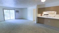 This single-floor residence features two bedrooms and one bathroom within a well-utilized floor plan. The open living and dining area is spacious and carpeted, providing a neutral, move-in-ready canvas with light-toned walls that brighten the space. A window unit air conditioner and a sliding glass door or large window allow for natural light and ventilation in the main living area, lending a sense of openness to the room.

Adjacent to the living space, the kitchen is accessible via a pass-through counter with a built-in breakfast bar, creating a convenient connection between the cooking and living areas. The kitchen features wood-toned upper cabinetry, a white range, and a mirrored backsplash element that adds depth to the compact cooking space. The textured ceiling throughout the home adds a classic architectural finish.

The overall layout is efficient and functional, with a straightforward flow between rooms. The neutral color palette and carpeted floors throughout the living area contribute to a clean, understated aesthetic. This residence is well-suited for those seeking a practical, comfortable home with a manageable footprint and essential amenities conveniently arranged across a single level.