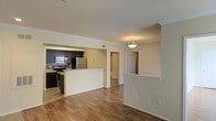 This single-floor residence showcases an open-concept design that integrates the kitchen and living areas into one cohesive space. The kitchen is outfitted with dark espresso cabinetry, stainless steel appliances including a refrigerator and range, and a mosaic tile backsplash that adds a decorative accent. A peninsula counter provides a natural boundary between the kitchen and the adjoining living space, making it ideal for casual dining or entertaining.

The flooring throughout is warm-toned hardwood-style planks, lending a consistent and inviting aesthetic across the main living areas. Crown molding runs along the upper walls and ceiling, adding a refined architectural detail that elevates the overall finish of the space.

A pendant light fixture is centrally hung in the living area, contributing to a well-lit and welcoming atmosphere. The neutral, light-toned walls complement the darker cabinetry and flooring, creating a balanced contrast. Hallway access visible from the main area leads to additional rooms, suggesting a functional and practical floor plan. Overall, the space presents a clean, modern aesthetic with thoughtful design details throughout.