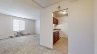 Located at 9235 N Church Dr in Parma Heights, Ohio, this 2-bedroom, 1-bathroom unit offers a practical and efficient single-floor layout. The living area is carpeted and benefits from natural light through a large sliding window, complemented by a wall-mounted air conditioning unit and baseboard heating. A ceiling fan adds to the comfort of the space. The kitchen is efficiently designed with wood-look vinyl flooring, white cabinetry, ample counter space, and a full-size refrigerator, accessed directly from the main living area. The primary bedroom is a well-proportioned carpeted room with a bright window fitted with blinds and baseboard heating. The second bedroom is also carpeted and connects to the hallway, which features hardwood-style flooring and closet access. The full bathroom is outfitted with a vanity with medicine cabinet, tile surround walls, a tub-shower combination, and a classic basket-weave tile floor. A ceiling fan is also present in the bathroom. Throughout the unit, clean white walls and neutral tones create a bright, cohesive atmosphere. Baseboard heating is consistent throughout the rooms, ensuring reliable climate control year-round.