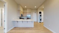 Located at 30 Country Club Rd in Eugene, Oregon, this single-floor residence offers a thoughtfully designed layout with modern finishes throughout. The open-concept kitchen serves as the heart of the home, featuring light wood cabinetry, a full suite of stainless steel appliances including a gas range, microwave, and French door refrigerator, and a generous peninsula with a built-in sink and breakfast bar seating — ideal for both cooking and casual dining. Light wood-tone flooring runs throughout the main living areas, lending warmth and continuity to the space. The living area extends toward a sliding glass door that opens onto a private balcony, offering expansive views of the Eugene skyline and surrounding landscape, with an additional window amplifying the natural light. A dedicated in-unit laundry closet with a stacked washer and dryer adds everyday convenience. The bedroom is carpeted and features a large window with scenic views and a wall-mounted climate control unit. The bathroom is well-appointed with light wood vanity cabinetry, a wide countertop, large mirrors, tile flooring, and a glass-enclosed walk-in shower. Clean, neutral tones and recessed lighting throughout create a bright, contemporary ambiance.