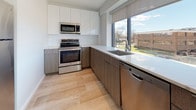 Unit 301 is a thoughtfully designed one-bedroom, one-bathroom residence that combines modern aesthetics with functional living. The layout, as revealed by the floor plan, flows efficiently from the living areas through to the private spaces, creating a cohesive and well-organized environment throughout.

The kitchen is a standout feature, outfitted with a full suite of stainless steel appliances including a refrigerator, electric range, built-in microwave, and dishwasher. Two-toned cabinetry pairs white upper cabinets with warm wood-grain lower cabinets, complemented by clean white countertops. Light wood-style flooring runs throughout, and a large window above the sink fills the space with natural light while offering outdoor views.

The bedroom is generously proportioned, featuring plush carpeting and oversized windows that frame views of the surrounding neighborhood and allow abundant natural light to brighten the room. A wall-mounted climate control unit adds convenience.

The bathroom maintains the home's contemporary character with wood-look tile flooring, a sleek white vanity, and a glass-enclosed walk-in shower finished with elegant gray stone-patterned tile, creating a clean and spa-like atmosphere.