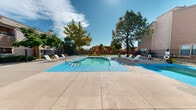 Located at 3901 Montgomery Blvd NE in Albuquerque, New Mexico, this two-story property showcases a well-appointed outdoor amenity area that serves as a central gathering space for residents. The exterior architecture reflects a Southwestern aesthetic, with warm earth-toned stucco facades, tiered balconies, and traditional rooflines that blend seamlessly into the Albuquerque landscape.

The highlight of the property is its generously sized outdoor swimming pool, featuring clear turquoise water and a surrounding concrete deck fitted with multiple lounge chairs — ideal for relaxing beneath New Mexico's abundant sunshine. Adjacent to the main pool sits a dedicated hot tub, offering a more intimate space for unwinding. The pool area is enclosed by a wrought iron security fence, providing both safety and an open feel.

Mature trees, including tall pines and shade trees, are thoughtfully distributed throughout the grounds, offering natural shade and greenery against the arid backdrop. A separate outdoor seating area with patio furniture provides additional space for socializing. Manicured green lawn areas are visible along the perimeter, adding a refreshing contrast to the desert environment. The two-story building wings flank the pool courtyard, creating a cohesive, community-centered layout that encourages outdoor living year-round.
