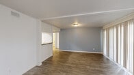 This single-story residence features four bedrooms and two bathrooms within a thoughtfully organized floor plan. Wood-style luxury vinyl plank flooring runs consistently throughout the home, lending a cohesive, clean aesthetic to every room.

The combined kitchen and living area forms the heart of the home. The kitchen is equipped with white cabinetry, granite-style countertops, a black appliance package including a refrigerator, dishwasher, and electric range, and a pass-through counter that opens toward the living space. The living room is generously sized, featuring soft blue-gray walls and a window that allows natural light to filter in.

The bedrooms are well-proportioned, with the primary bedroom offering comfortable dimensions and access to a dedicated closet space featuring dual shelving rods. One bedroom includes a large sliding glass door that opens to an outdoor view, providing additional natural light. The bathrooms feature granite-style countertops, undermount sinks, and illuminated vanity mirrors. Two hallways connect the private and common areas efficiently. Throughout the home, white walls and light flooring create a bright, neutral ambiance.