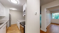 This well-appointed one-bedroom, one-bathroom unit offers a thoughtfully organized layout across a single floor. Warm hardwood flooring flows throughout the space, creating a cohesive and inviting atmosphere. The open kitchen and living area form the heart of the unit, where a peninsula with bar seating serves as both a functional workspace and a casual dining spot. The kitchen is outfitted with sleek white cabinetry, light stone countertops, a stainless steel refrigerator, a built-in microwave, and an electric range — all contributing to a clean, modern aesthetic. A textured ceiling and flush-mount lighting add subtle character throughout. The bedroom is a comfortable retreat featuring a large window that frames lush, verdant tree views and a baseboard heating system. A dedicated closet provides practical storage. The bathroom is well-equipped with a wide vanity topped with a stone-toned countertop, white cabinetry with modern hardware, a large mirror with overhead lighting, and a shower. A private balcony off the living area overlooks a dense, mature tree canopy, offering a peaceful natural backdrop and a quiet outdoor escape. A wall-mounted thermostat provides convenient climate control throughout the unit.