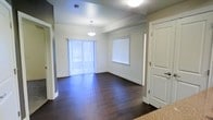 This single-floor space showcases a clean, contemporary design centered around an open-concept living and dining area. The room is anchored by rich, dark hardwood flooring that runs throughout, creating a warm contrast against the neutral light-grey walls and crisp white baseboards and trim.

Natural light is a defining feature of this space. A large sliding glass door dressed with vertical blinds dominates one wall, allowing an abundance of daylight to flood the interior. A secondary window with horizontal blinds further enhances the bright and airy atmosphere of the room.

A pendant light fixture hangs centrally above the dining area, providing focused overhead illumination and adding a subtle decorative touch to the space. The textured ceiling adds a modest architectural detail overhead.

Doorways visible from the main area suggest connectivity to additional rooms, offering a practical and functional layout. The overall ambiance is clean, open, and move-in ready, with a neutral palette that provides a versatile backdrop suitable for a variety of interior design styles.
