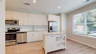 Located at 2020 W Morehead St in Charlotte, NC, this single-floor unit offers a thoughtfully designed, open layout with modern finishes and a light, airy atmosphere. The kitchen serves as a central highlight, featuring crisp white cabinetry extending to the ceiling for ample storage, a classic subway tile backsplash, light-toned countertops, and a full suite of stainless steel appliances including a French door refrigerator with ice maker, electric range, microwave, and dishwasher. A mobile kitchen island with a built-in drawer and lower shelving provides additional prep and storage flexibility. Light wood-tone luxury vinyl flooring runs throughout the space, lending warmth and continuity. The open living and dining area is bathed in natural light from multiple windows fitted with blinds, and is completed by a ceiling fan overhead. The bathroom is finished with full subway tile surrounding the soaking tub and shower combination, complemented by light wood-tone flooring and a vanity with clean-lined cabinetry. A walk-in closet with wire shelving is conveniently accessible directly from the bathroom. Neutral wall tones, recessed lighting, and consistent modern finishes throughout contribute to a cohesive and inviting atmosphere.
