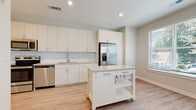 Located at 2020 W Morehead St in Charlotte, NC, this single-floor unit offers a thoughtfully designed, open layout with modern finishes and a light, airy atmosphere. The kitchen serves as a central highlight, featuring crisp white cabinetry extending to the ceiling for ample storage, a classic subway tile backsplash, light-toned countertops, and a full suite of stainless steel appliances including a French door refrigerator with ice maker, electric range, microwave, and dishwasher. A mobile kitchen island with a built-in drawer and lower shelving provides additional prep and storage flexibility. Light wood-tone luxury vinyl flooring runs throughout the space, lending warmth and continuity. The open living and dining area is bathed in natural light from multiple windows fitted with blinds, and is completed by a ceiling fan overhead. The bathroom is finished with full subway tile surrounding the soaking tub and shower combination, complemented by light wood-tone flooring and a vanity with clean-lined cabinetry. A walk-in closet with wire shelving is conveniently accessible directly from the bathroom. Neutral wall tones, recessed lighting, and consistent modern finishes throughout contribute to a cohesive and inviting atmosphere.