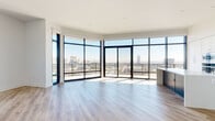 This high-rise residence offers four bedrooms and four bathrooms across a generously sized single-floor layout, combining modern design with sweeping urban panoramas. The open-concept kitchen and living area serves as the heart of the home, featuring light wood-tone flooring, white shaker cabinetry, a bold navy kitchen island, decorative tile backsplash, and stainless steel appliances. Corner floor-to-ceiling glass walls flood the living space with natural light and frame breathtaking city skyline views, with direct access to a private balcony. Each bedroom is well-proportioned, with large windows capturing elevated cityscape vistas and continuing the light hardwood flooring throughout. The spacious primary bedroom includes an expansive walk-in closet outfitted with built-in shelving and hanging rods. The four bathrooms are elegantly finished with marble-style tile flooring and wall surrounds, undermount sinks, and contemporary vanities. A dedicated laundry room provides full-size side-by-side washer and dryer units alongside ample white cabinetry and counter space. The hallway features a distinctive tray ceiling detail, adding architectural character to the interior. With three closets, a welcoming entrance, and refined finishes throughout, this residence delivers a polished, high-elevation urban living experience.
