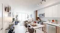 This single-floor residence showcases a thoughtfully designed open-concept layout that seamlessly connects the kitchen, dining, and living areas. The kitchen is outfitted with two-tone cabinetry—combining crisp white upper cabinets with warm wood-toned lower units—complemented by a herringbone-patterned tile backsplash, light quartz countertops, and a full suite of stainless steel appliances including a range, microwave, dishwasher, and refrigerator. A compact dining table with modern upholstered chairs sits adjacent to the kitchen, creating a natural transition into the open living space.

The living area benefits from floor-to-ceiling windows dressed with sheer roller shades, flooding the space with abundant natural light while maintaining privacy. Light wood-toned flooring runs throughout the main living areas, contributing to the home's airy, contemporary feel. Track lighting accents the kitchen and dining zones overhead.

Both bedrooms feature large black-framed windows with urban views, light flooring, and clean white walls that create a calm, restful atmosphere. The full bathroom is finished with large-format neutral floor tiles, dark wood-toned vanity cabinetry, a white countertop, and a soaking tub with shower combination, offering a clean and functional design.