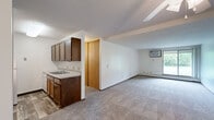 This single-floor unit in Sioux Falls, SD offers a straightforward and functional layout with two bedrooms, one bathroom, and two closets. The open-concept living and dining area is generously proportioned, featuring neutral carpet flooring, white walls, and a textured ceiling throughout. A wall-mounted air conditioning unit and baseboard heating ensure year-round comfort, while a sliding glass door at the end of the living area invites natural light and provides outdoor access. A ceiling fan adds to the room's practicality.

The kitchen is positioned adjacent to the living area in a semi-open arrangement, featuring dark wood cabinetry, a countertop sink, and white appliances, offering efficient use of the available space. A sliding wood-panel closet door provides convenient storage nearby.

The primary bedroom is a well-sized, carpeted room with a window fitted with blinds, allowing for natural light while maintaining privacy. Baseboard heating runs along the wall. The second bedroom is equally functional, finished with the same neutral carpet and clean white walls.

The bathroom is neatly appointed with wood-look tile flooring, a white vanity with under-cabinet storage, a full tub-shower combination with grab bars, and crisp white finishes throughout, creating a clean and accessible space.
