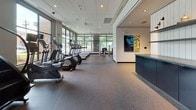 This single-floor fitness center in Atlanta, GA (30318) offers a thoughtfully designed workout environment spread across several distinct functional zones. The main cardio area is lined with large floor-to-ceiling windows that frame views of mature trees and brick exterior walls, flooding the space with natural light. Rows of ellipticals, stair climbers, and treadmills are arranged to take full advantage of the outdoor views, while mounted flat-screen televisions provide entertainment during workouts. Durable rubberized flooring throughout ensures safety and comfort underfoot.

The strength training zone features a variety of cable machines, weight benches, and resistance equipment positioned alongside expansive glass walls and mirrors that amplify the sense of space. Ceiling fans and recessed lighting maintain a bright, well-ventilated atmosphere.

A dedicated cycling and studio room is enclosed by sleek floor-to-ceiling frosted glass partitions, creating a semi-private space for spin bikes and rowing machines, complete with its own television display. An additional multipurpose room accommodates group fitness activities, outfitted with spin bikes, stability balls, and a mounted screen.

A central corridor with white shiplap-paneled walls and built-in shelving connects the zones, lending a clean, modern aesthetic. The overall design balances functionality with contemporary style, making this fitness center a well-rounded facility for a wide range of training needs.
