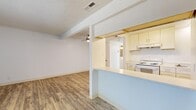 This single-floor residence offers three bedrooms, two bathrooms, and a thoughtfully arranged layout that maximizes functionality. The living room serves as a welcoming entry point, featuring durable wood-look laminate flooring, a textured ceiling, and a ceiling fan that enhances airflow and comfort. A large window dressed with vertical blinds fills the space with natural light and provides a view of the greenery outside.

The kitchen flows seamlessly from the living area via a peninsula-style breakfast bar with a light blue accent, creating an open and connected feel. White cabinetry lines the kitchen walls, paired with a white appliance suite and a built-in range. The layout offers generous counter space and practical storage through upper and lower cabinets.

The three bedrooms are carpeted and bright, each featuring windows with vertical blinds that invite natural light. The primary bedroom is a comfortable size and includes its own closet. Additional closets throughout the unit provide ample storage for all occupants.

The bathrooms are clean and functional, with wood-look flooring and sliding glass shower enclosures. A hallway connects the private sleeping quarters, creating a clear separation between the living and bedroom areas. Overall, the space presents a clean, neutral palette throughout, making it move-in ready and easy to personalize.