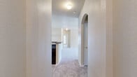 This single-story, 3-bedroom, 2-bathroom home offers a thoughtfully designed layout that maximizes comfort and functionality. The entrance opens through a hallway with a distinctive arched architectural detail, leading into a combined kitchen and living area. The kitchen features warm wood cabinetry, dark granite-style countertops with a breakfast bar peninsula, and a black appliance suite, all illuminated by bright overhead lighting. The adjoining living room is generously sized, featuring plush neutral carpeting, a ceiling fan, and a set of windows with a glass door that invites abundant natural light and outdoor views. A decorative wainscoting accent adds character to the dining area. The three bedrooms are carpeted and well-proportioned, with the spacious primary bedroom offering ample room to furnish. Each bedroom benefits from large windows with exterior views and ceiling fans for year-round comfort. Both bathrooms are finished with wood-toned cabinetry, dark countertops, and a tub-shower combination, with one bathroom featuring warm hardwood-style flooring. Textured walls throughout the home add a layer of visual interest, and the neutral color palette creates a clean, inviting ambiance across every room.