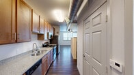 Located at 2604 Aldrich St in Austin, TX, this efficient single-floor unit offers a well-designed layout that maximizes functionality within its compact footprint. The open-plan living area features rich, dark hardwood-style flooring that extends throughout the entire space, creating a cohesive and modern aesthetic. A ceiling fan provides comfort and light to the living area, which benefits from natural light through a large window.

The galley-style kitchen is a standout feature, outfitted with warm-toned wood cabinetry offering generous upper and lower storage. Granite-look countertops provide ample prep space, while stainless steel appliances — including a gas range, microwave, refrigerator, and dishwasher — deliver a fully equipped cooking experience. An exposed industrial-style ductwork runs overhead, adding a loft-like character to the kitchen corridor. A peninsula with upper cabinetry separates the kitchen from the living area, offering an open yet defined transition between the two spaces.

The bathroom is clean and straightforward, featuring a glass-enclosed walk-in shower with modern brushed nickel fixtures set against crisp white walls. Throughout the unit, the design balances industrial touches with practical, everyday livability, making it a functional and characterful space in the heart of Austin.