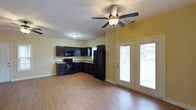 This single-story carriage home at Vineland Carriage Homes offers an open and functional layout designed for comfortable everyday living. The main living area flows seamlessly into the kitchen, creating a connected and airy feel throughout the space. Warm hardwood-style flooring extends across the main area, adding a clean and cohesive aesthetic underfoot.

The kitchen is equipped with dark espresso cabinetry that provides a bold contrast against the light yellow walls. Black appliances, including a gas range, over-the-range microwave, and a French door refrigerator, complement the cabinetry for a uniform, contemporary look. Stone-style countertops add a practical and attractive workspace for cooking and meal preparation. The kitchen is positioned in an L-shaped configuration, making efficient use of the available space.

A ceiling fan with a light fixture is centrally located in the main living area, offering both air circulation and ambient lighting. Natural light fills the space through a set of French doors, which provide direct access to the outdoors and offer views of the surrounding exterior. The textured ceiling and neutral wall tones contribute to a bright and welcoming overall atmosphere throughout the home.