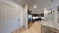 This contemporary single-floor residence showcases a thoughtfully designed open-concept layout with high-end finishes throughout. The kitchen serves as the centerpiece of the living space, featuring striking dark cabinetry that extends to the ceiling, a full suite of stainless steel appliances including a French door refrigerator with ice maker, built-in microwave, and range. A generously sized granite island with an undermount sink and pendant lighting above provides both a functional workspace and a natural gathering point. Light wood-style flooring flows throughout the main living areas, complementing the neutral color palette.

The bedrooms offer plush carpeting for added comfort, with windows that invite natural light into each room. One bedroom features an en-suite bathroom and walk-in closet, providing added privacy and convenience. The bathrooms are finished with granite-topped dark wood vanities, large-format tile surround, a soaking tub, and a glass-enclosed shower, delivering a polished, spa-like aesthetic. A well-appointed entryway with a modern paneled front door and keypad entry provides a welcoming and secure arrival experience. Recessed lighting and ceiling fan fixtures are featured throughout, completing this clean, modern interior.