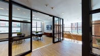 Located at 66 Summer St in downtown Stamford, Connecticut, this thoughtfully designed amenity floor offers a refined blend of functionality and modern aesthetics. Light bamboo-toned hardwood flooring flows throughout the space, providing a warm, cohesive foundation that ties the various areas together seamlessly.

The floor features glass-partitioned conference and meeting rooms enclosed by sleek black-framed floor-to-ceiling glass walls and sliding doors, allowing natural light to penetrate deep into the interior while maintaining acoustic privacy. Each meeting room is equipped with a wall-mounted display and a conference table surrounded by modern seating, making them well-suited for both collaborative and formal gatherings.

A lounge-style area offers a more relaxed setting, furnished with a tufted leather armchair, a large conference table with contemporary chairs, and a tall indoor plant that adds a touch of greenery. Framed abstract artwork adorns the walls, contributing to the space's polished, professional character.

A dedicated fitness room is outfitted with strength training equipment, cardio machines, and natural light from street-facing windows, providing a convenient wellness amenity within the building.

Recessed ceiling lighting and a drop-panel ceiling system maintain a clean, corporate finish throughout. Views of the surrounding Stamford streetscape are visible through large, grid-paned windows, grounding the space in its vibrant urban context.