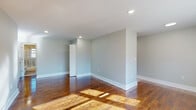 This single-floor space offers a clean, modern aesthetic defined by rich, polished hardwood floors that flow seamlessly throughout. The main living area is open and airy, bathed in natural light streaming through large windows, and illuminated overhead by recessed lighting set into smooth white ceilings. Soft gray walls provide a neutral, versatile backdrop across all rooms.

The kitchen is thoughtfully updated, featuring gray shaker-style cabinetry, white quartz countertops, a classic subway tile backsplash, and stainless steel appliances including a gas range and over-the-range microwave. A stainless steel sink completes the functional layout.

The bedrooms are generously sized, each with gleaming hardwood floors, soft gray walls, and ample natural light from well-placed windows. One bedroom features a wall-mounted HVAC unit and baseboard heating along with views of the surrounding area. A louvered closet door adds a practical storage element to the living spaces.

The bathroom maintains the cohesive modern style of the unit, showcasing a dark-toned vanity with a white countertop, a brushed nickel faucet and fixtures, and a large mirror. The space is bright and clean, connecting directly to the hardwood-floored hallway. Overall, this space combines timeless materials with contemporary finishes for a polished, move-in-ready feel.
