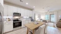 This thoughtfully designed 2-bedroom, 3-bathroom single-story residence offers a bright, modern aesthetic with a cohesive palette of crisp whites and warm natural wood tones. Light hardwood flooring flows seamlessly throughout, enhancing the open, airy feel of the space.

The open-concept kitchen is a standout feature, outfitted with sleek white shaker cabinetry, a white tile backsplash, stone countertops, and a full suite of stainless steel appliances including a range, over-range microwave, dishwasher, and French-door refrigerator. A natural wood dining table positioned at the kitchen's edge creates a smooth transition into the living area.

The living room is welcoming and well-lit, benefiting from a ceiling fan and direct access to the outdoors through a glass door that invites natural light. The spacious primary bedroom features vaulted ceilings and direct access to an en-suite bathroom with dual vanities, white cabinetry, and stone countertops. A generous walk-in closet with multi-level wire shelving provides ample storage.

The second bedroom is well-proportioned with its own closet and access to a full bathroom featuring a single vanity with quartz countertops. A third bathroom rounds out the home. Throughout, the design maintains a calm, neutral ambiance ideal for comfortable everyday living.