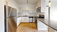 Located in Seattle's Greenwood neighborhood, this 1-bedroom, 2-bathroom unit offers a thoughtfully designed, single-floor layout that maximizes functionality. The open-concept living, dining, and kitchen area forms the heart of the space, featuring hardwood-style flooring that flows throughout and large sliding glass doors that flood the area with natural light and provide access to a private balcony with views of surrounding greenery.

The kitchen is well-equipped with stainless steel appliances, including a range, over-the-range microwave, dishwasher, and refrigerator. White cabinetry, gray countertops, and a classic subway tile backsplash give the kitchen a clean, modern aesthetic. A peninsula with pendant lighting serves as both a workspace and a casual dining area connecting the kitchen to the living space.

The bedroom is a comfortable, bright room with its own sliding glass door to the balcony, offering a peaceful outdoor connection. The unit includes two full bathrooms, each finished with white tile flooring and a tub/shower combination. Additional conveniences include in-unit laundry and a dedicated closet. The consistent use of white walls, dark door trim accents, and wood-tone flooring throughout gives the space a cohesive, contemporary feel.
