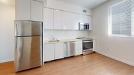 Located on the iconic Wilshire Boulevard in the heart of Los Angeles, this one-bedroom, one-bathroom unit offers a clean, modern aesthetic throughout. Light wood-tone flooring runs continuously across the single-floor layout, lending warmth and visual cohesion to the space.

The open living area is bright and airy, with crisp white walls and dual windows fitted with horizontal blinds that allow natural light to filter in while offering city views. The contemporary kitchen features a streamlined galley design with sleek white cabinetry, light countertops, a tile backsplash, and a full suite of stainless steel appliances including a refrigerator, range, microwave, and dishwasher.

The bedroom is a comfortable, well-proportioned retreat with its own window for natural light and a generous sliding-door closet providing ample storage. An additional closet is conveniently accessible just outside the bathroom entry.

The bathroom is finished with large-format neutral stone-look tile surrounding a full soaking tub and shower combination, complemented by wood-tone flooring that ties the space together. In-unit laundry hookups are also present, as visible in the layout. The overall design is modern and minimalist, making for a functional and well-appointed urban residence.