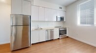 Located on the iconic Wilshire Boulevard in the heart of Los Angeles, this one-bedroom, one-bathroom unit offers a clean, modern aesthetic throughout. Light wood-tone flooring runs continuously across the single-floor layout, lending warmth and visual cohesion to the space.

The open living area is bright and airy, with crisp white walls and dual windows fitted with horizontal blinds that allow natural light to filter in while offering city views. The contemporary kitchen features a streamlined galley design with sleek white cabinetry, light countertops, a tile backsplash, and a full suite of stainless steel appliances including a refrigerator, range, microwave, and dishwasher.

The bedroom is a comfortable, well-proportioned retreat with its own window for natural light and a generous sliding-door closet providing ample storage. An additional closet is conveniently accessible just outside the bathroom entry.

The bathroom is finished with large-format neutral stone-look tile surrounding a full soaking tub and shower combination, complemented by wood-tone flooring that ties the space together. In-unit laundry hookups are also present, as visible in the layout. The overall design is modern and minimalist, making for a functional and well-appointed urban residence.