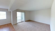 This single-floor residence features two bedrooms and two bathrooms within a well-proportioned layout designed for comfortable everyday living. The living area is a highlight of the space, showcasing vaulted ceilings that lend an open, airy feel and enhance the sense of volume throughout the room. Neutral-toned wall-to-wall carpeting adds warmth underfoot, while the clean white walls provide a bright, versatile backdrop. A sliding glass door leads directly to a private balcony, inviting natural light deep into the living space and offering a convenient indoor-outdoor connection. The balcony features a classic railing and provides a pleasant area for outdoor relaxation. The transition from carpet to hard flooring visible at the room's edge suggests distinct zones within the home, adding functional variety to the layout. The overall aesthetic is clean, neutral, and move-in ready, making it easy to personalize. The combination of vaulted ceilings, natural light, and private outdoor access creates an inviting atmosphere throughout this thoughtfully arranged two-bedroom home.